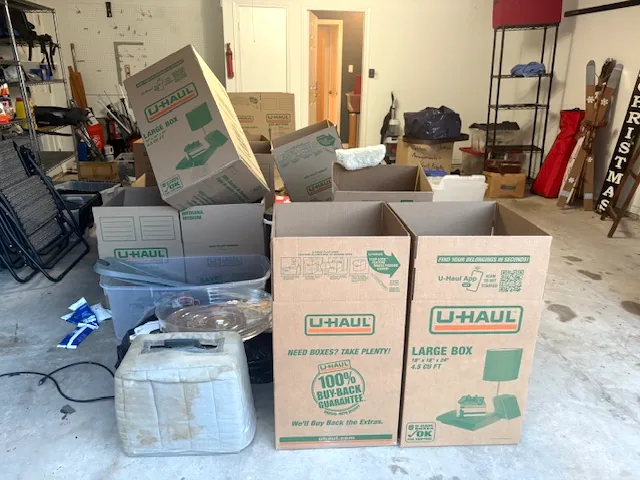 A two-car garage floor covered in moving boxes, bins and chairs