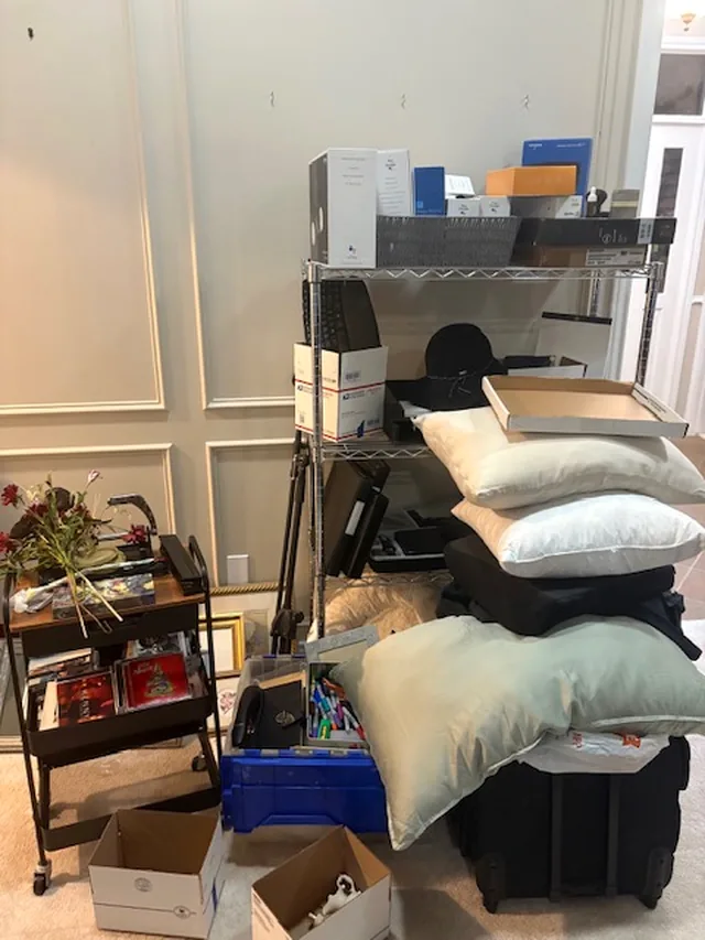 A living room with a wire shelf stacked with pillows, boxes and suitcases