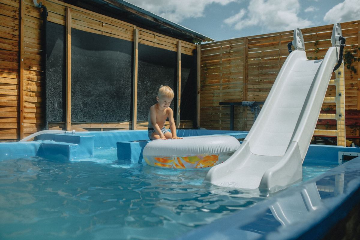 An above-ground pool with a slide inside a fenced backyard