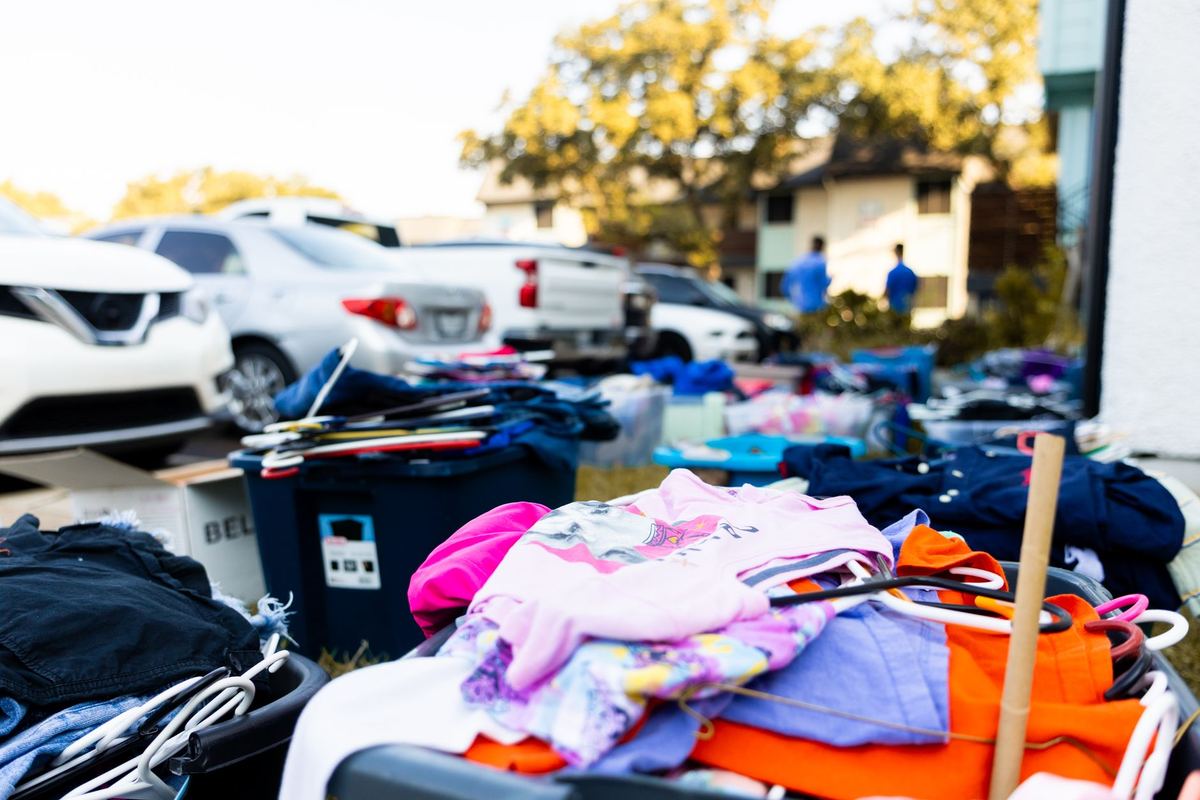 Unsold clothes, hangers and storage bins left out on a lawn at the end of a yard sale