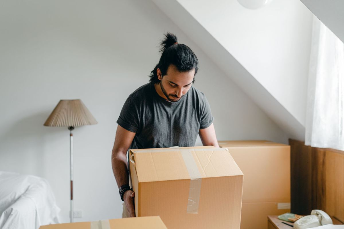 A man lifting a cardboard box in an attic room under a sloped ceiling