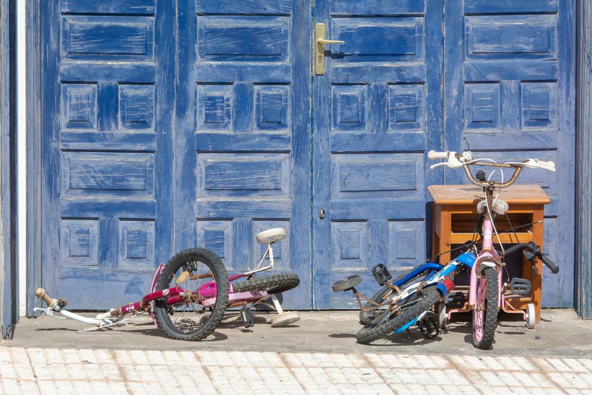 Two outgrown children's bicycles lying in front of a blue garage door