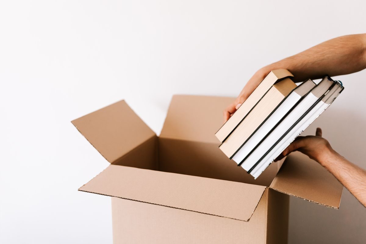 Hands packing a stack of hardcover books into a cardboard box