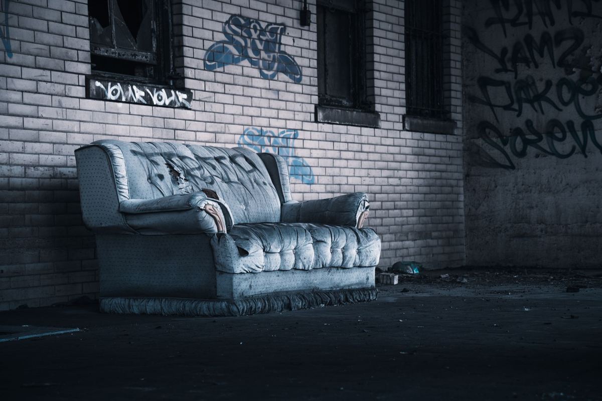 A worn upholstered sofa left out against a brick wall