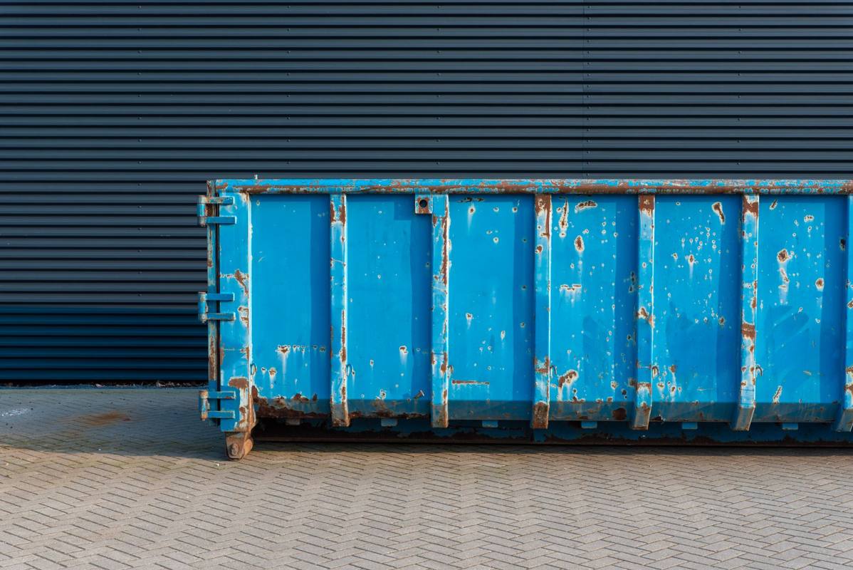 A blue roll-off dumpster parked against a building