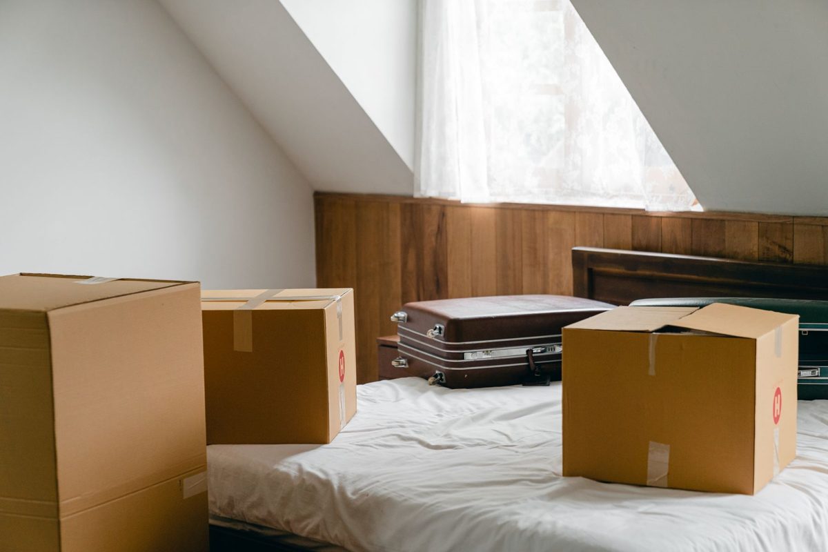 Moving boxes and old suitcases on a bed in a bright, mostly empty bedroom
