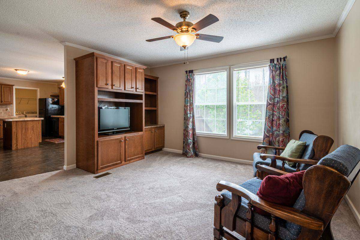 A wood entertainment center wall unit with a TV and side shelves in a carpeted living room