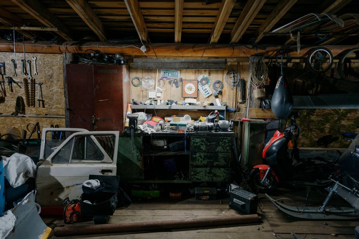 A cluttered garage with tools on the wall and parts on the floor