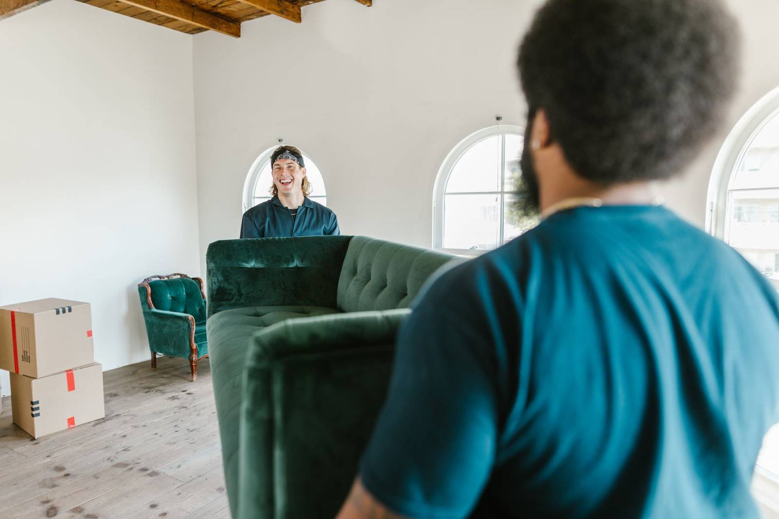 two movers carrying a green couch through a sunlit room past packed moving boxes