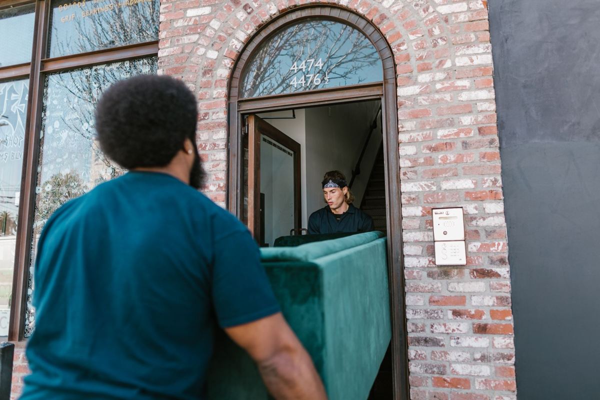 A worker carrying a sofa out through a brick doorway