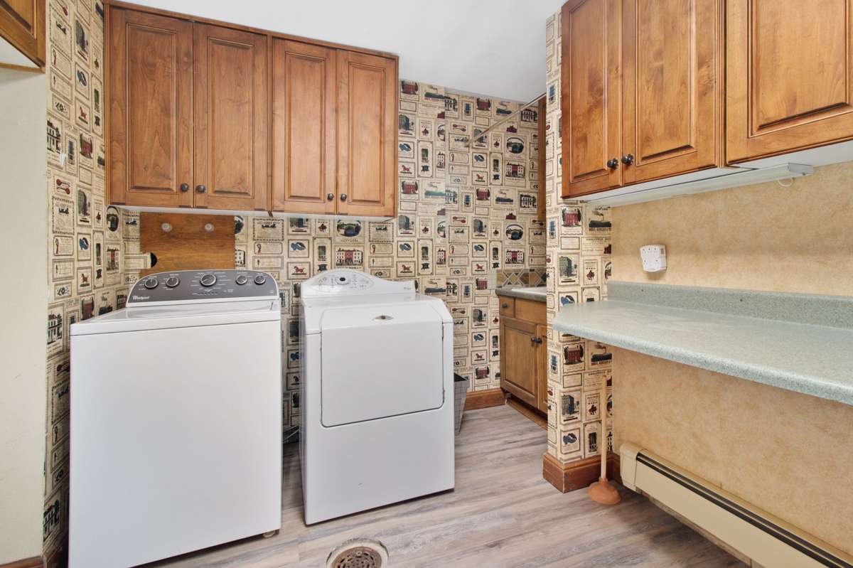 An older white top-load washer and dryer side by side in a laundry room with wood cabinets